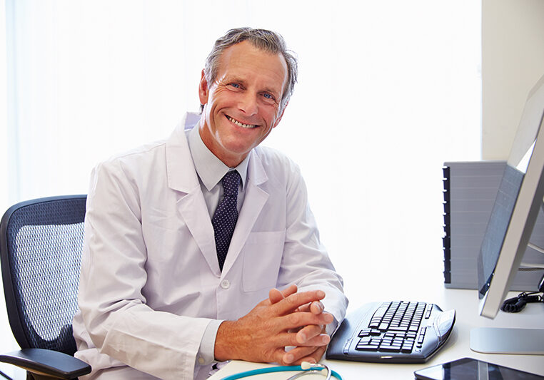 Portrait Of Male Doctor In Office Working At Computer Portrait Of Male Doctor In Office Working At Computer